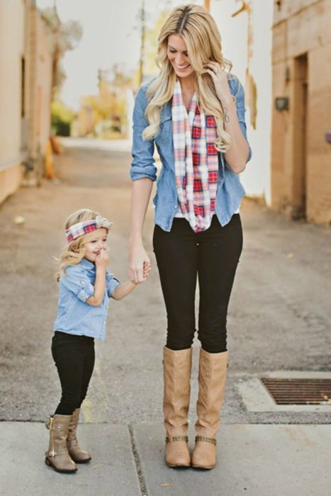 Madre e hija tomadas de la mano, llevando outfits iguales con jeans oscuros, botas altas y camisas a cuadros