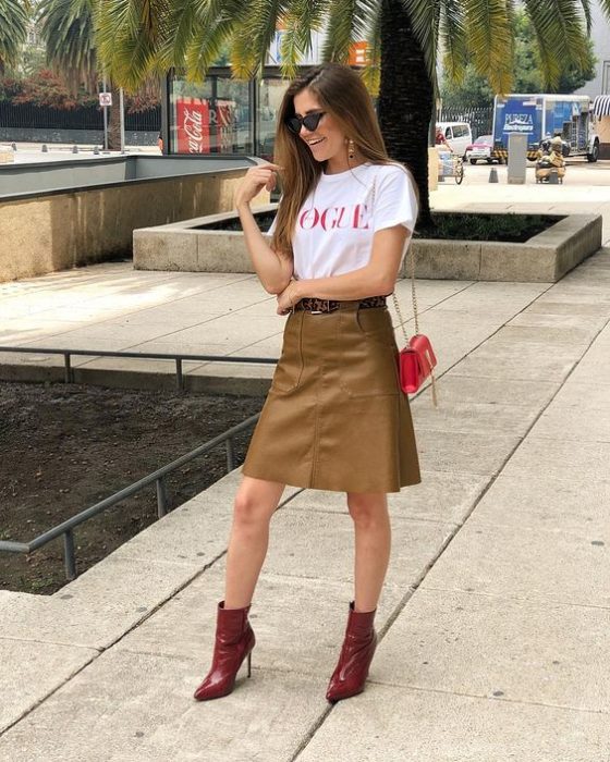 Chica usando una falda de color camel, botines rojos y camisa blanca