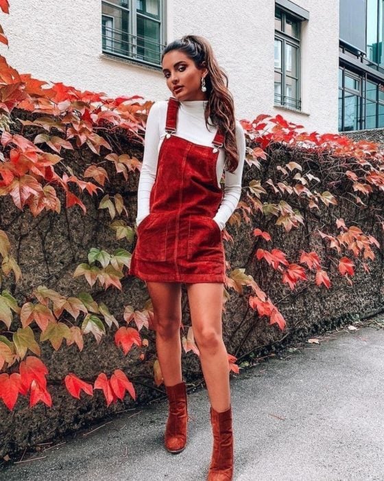 Outfits para otoño; chica de cabello castaño con peinado de coleta de caballo, con overol rojo de pana sobre blusa blanca de manga larga y cuello de tortuga, con botines rojos