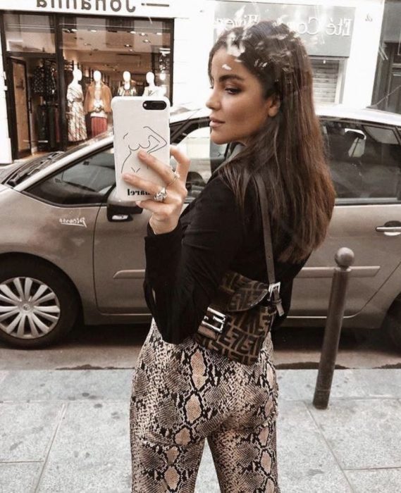 Outfits para otoño; chica tomándose selfie frente a aparador, con blusa negra y leggins de animal print de serpiente