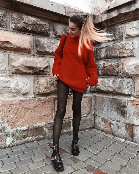 Outfits para otoño; chica con peinado de cola de cabello alta, con suéter oversized rojo usado como vestido, con medias de puntos y botines de trabajo con hebillas