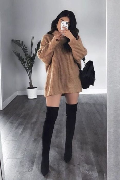 Chica usando un vestido estilo suéter de color café con botas altas de color negro 