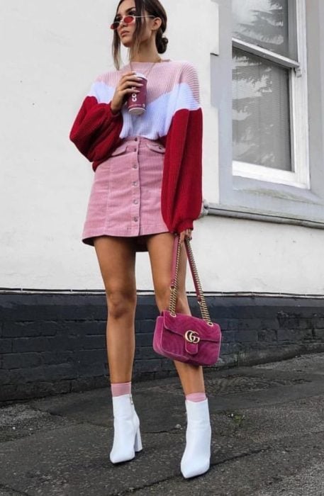 Chica usando una minifalda y un sueter de color rosa y botas blancas 