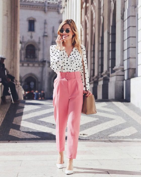 Chica usando un pantalón de color rosa con una blusa de lunares negros 