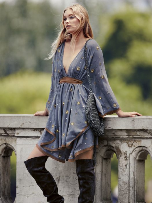 Ropa de constelaciones; mujer rubia con estilo boho, vestido hippie holgado color azul con estrellas amarillas y botas largas