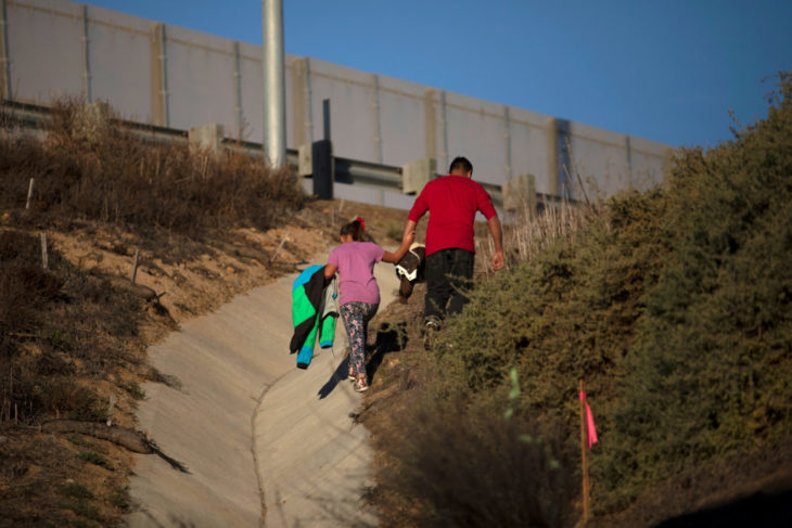 Un hombre lleva de la mano a su hija a un lado del muro fronterizo entre México y Estados Unidos