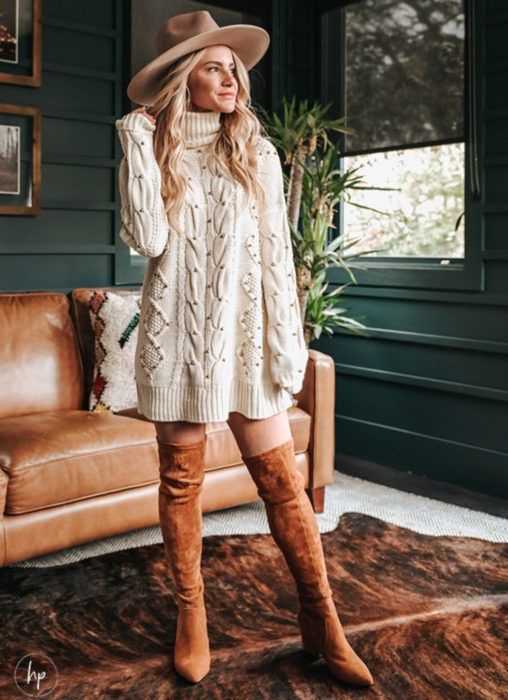 Chica rubia con sombrero estilo vaquero, suéter oversized tejido con cuentas usado como vestido de otoño, con botas largas anaranjadas de gamuza