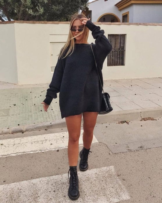 Chica cruzando la calle, con suéter oversized gris como vestido corto de otoño, con botas de trabajo Dr. Martens 