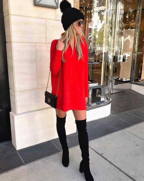 Chica rubia con gorro negro tejido de invierno, usando un suéter holgado rojo como vestido de otoño con mangas, botas negras largas