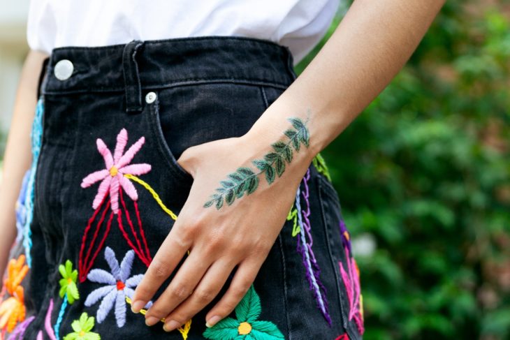 Chica mostrando un tatuaje temporal de Tessa Perlow con efecto bordado en forma de hojas d eeucalipto en la palma de la mano