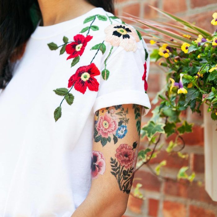 Chica mostrando su brazo con un tatuaje temporal de Tessa Perlow con efecto bordado en forma de flores de colores