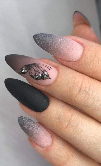 Chica con unas uñas de mariposa en colores negro con gris y brillos 