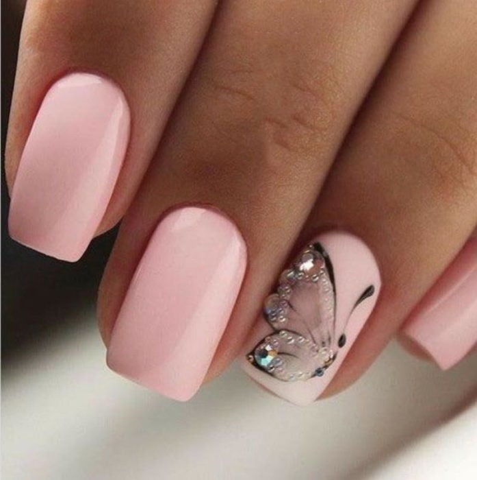 Chica con unas uñas de mariposa en color rosa y brillos de color tornasol 