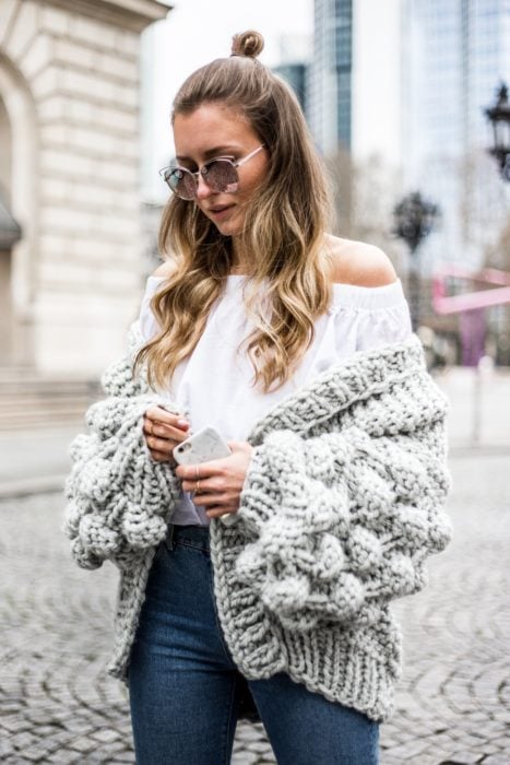 Chica caminando por la calle y usando un abrigo de lana tejido, jeans y blusa campesina de color blanco 