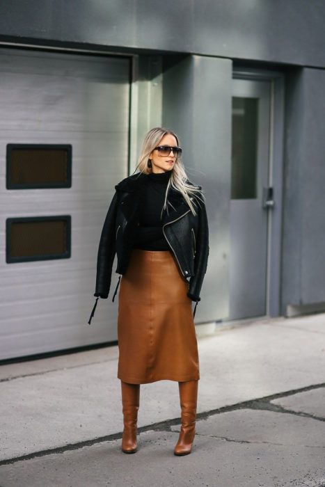 Chica usando una falda de cuero color café y botas, con chamarra de cuero y suéter negro