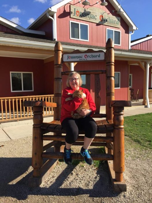 Melissa Blake sentada en una gran mecedora de madera afuera de una casa de madera