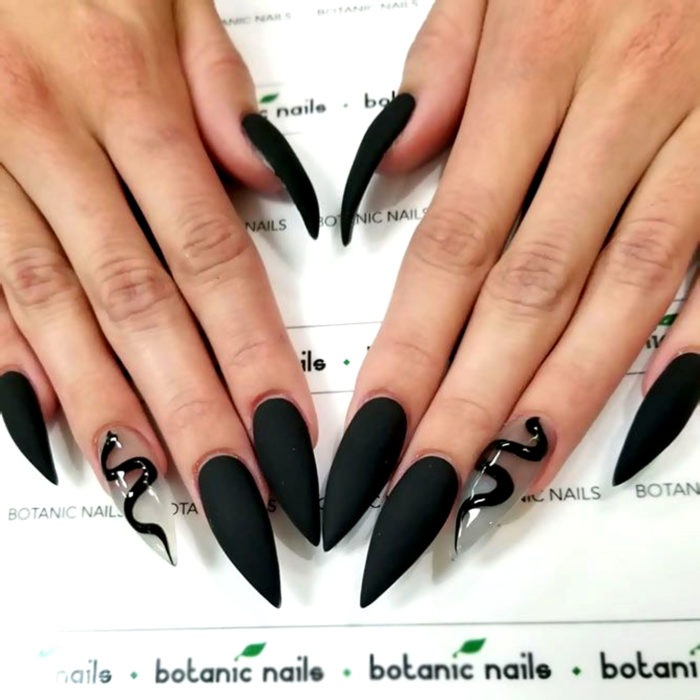 Uñas largas en forma stiletto, color negro mate con una uña transparente con dibujo de serpiente