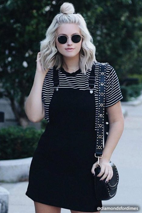 Chica parada en la calle mientras usa un vestido pichi de color negro y una blusa de color negro con líneas blancas 