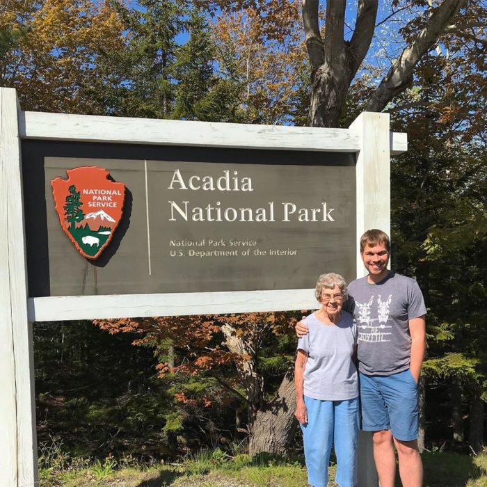 Brad y su abuela a un lado del letrero del Parque Nacional Acadia