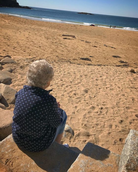 Joy, la abuela de Brad sentada en la playa viendo hacia el mar