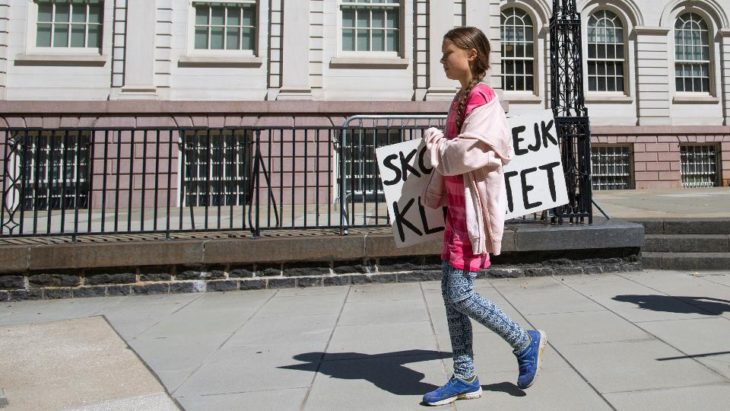 Greta Thunberg camina por una acera con un cartel bajo el brazo y un edificio de fondo