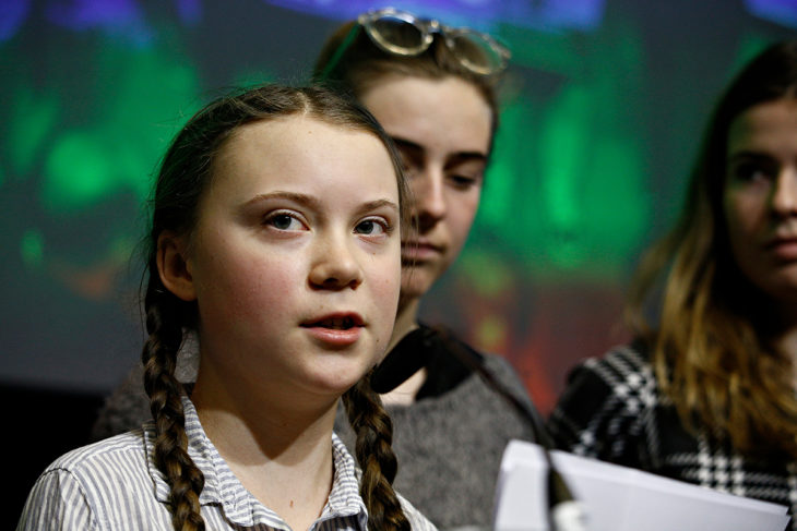 Greta Thunberg lee de una hoja frente a un micrófono, con camisa de cuadros