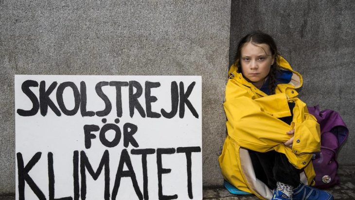 Greta Thunberg sentada en una banqueta con un letrero de su protesta de los viernes