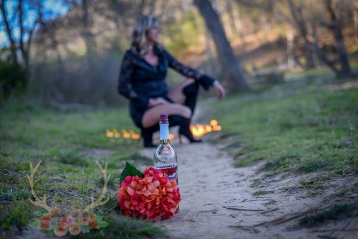 en primer plano un ramo de flores y una botella de vino, en segundo plano Marie Lollis en cluquillas