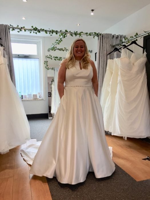 Una mujer con un vestido de novia en una tienda de vestidos, tiene las manos dentro de las bolsas