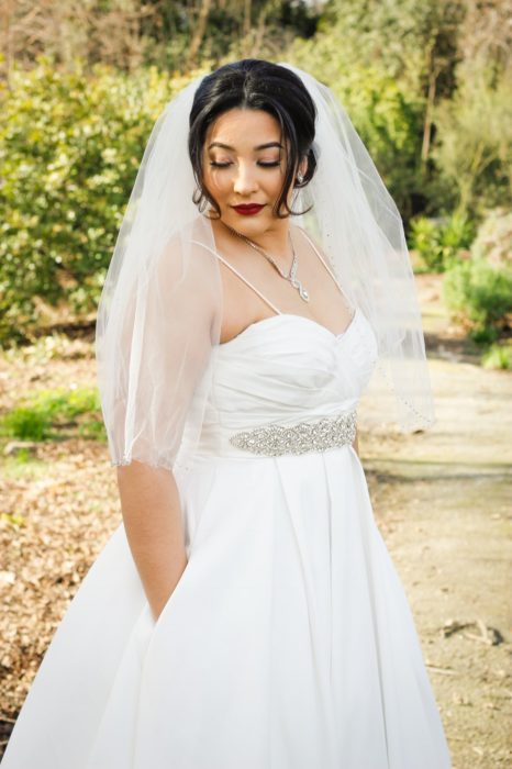 una novia posa en un jardín, con las manos dentro de las bolsas de su vestido