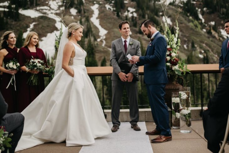 una ceremonia matrimonial, el novio lee un papel mientras que la novia lo mira con las manos dentro de las bolsas de su vestido