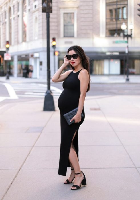 Chica embarazada posando para una sesión de fotos mientras usa un vestido negro largo con escote en una pierna 