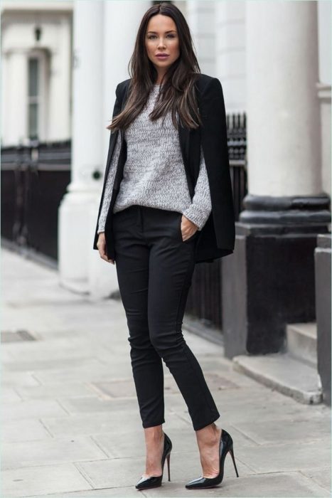 Chica usando un atuendo negro con un sueter de color gris mientras está parada en la calle 