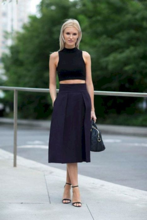 Chica usando una falda midi con un crop top de color negro mientras está parada en la calle 