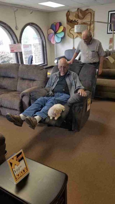 Abuelo recostado en un sofá reclinado mientras su perrito puddle está sentado al final del sofá 