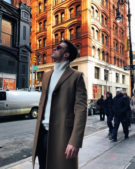 Actor Alemán usando una gabardina de color café y camisa de cuello de tortuga mientras está viendo hacia el cielo en Alemania 