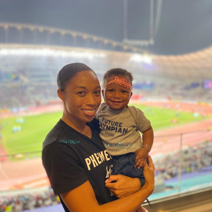 Allyson Felix cargando en brazos a su hija mientras están en un estadio