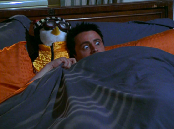 Joey Tribbiani asustado bajo las cobijas con su peluche de pingüino