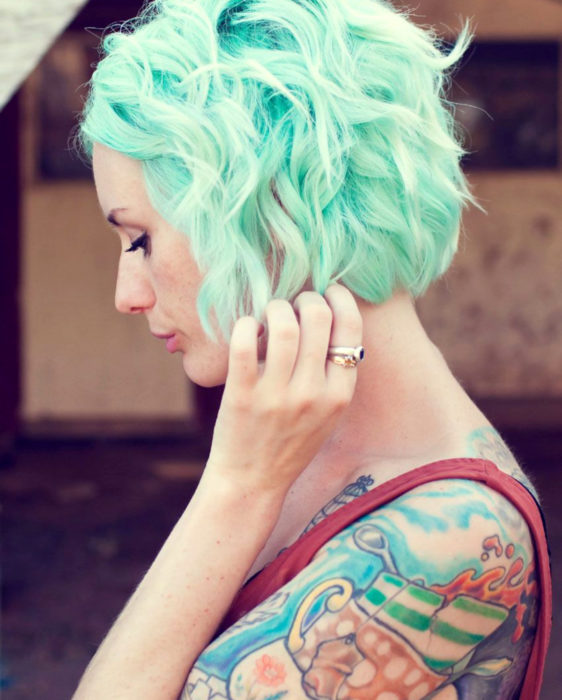 Tinte color verde menta; chica de cabello corto pixie ondulado con tatuajes en el brazo