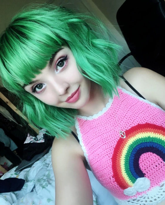 Tinte color verde menta; chica de ojos verdes con crop top tejido con estampado de arcoíris, de cabello corto arriba de los hombros, ondulado con fleco