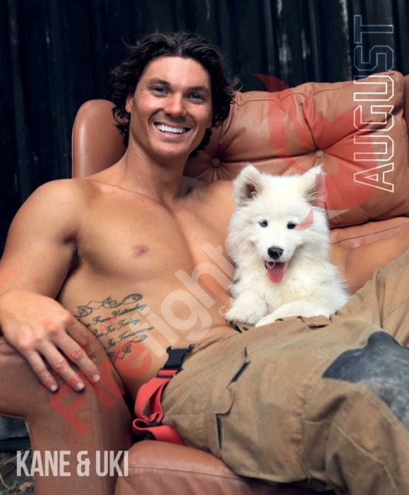 Calendario de bomberos australianos con animales; hombre con tatuaje sentado en un sillón con un perro cachorro husky blanco