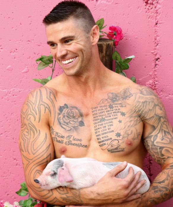 Calendario de bomberos australianos con animales; hombre con tatuajes, sonriendo y cargando a un cerdo, lechón