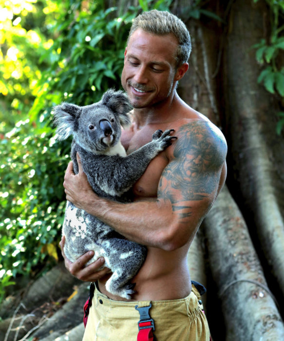 Calendario de bomberos australianos con animales; hombre de ojos azules cargando a un koala