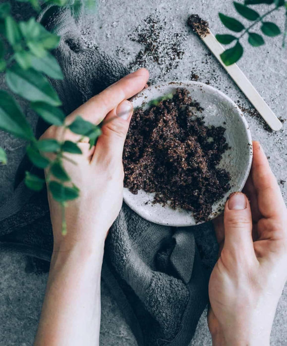 Razones por las que las axilas se oscurecen; mujer con recipiente con mascarilla exfoliante de café