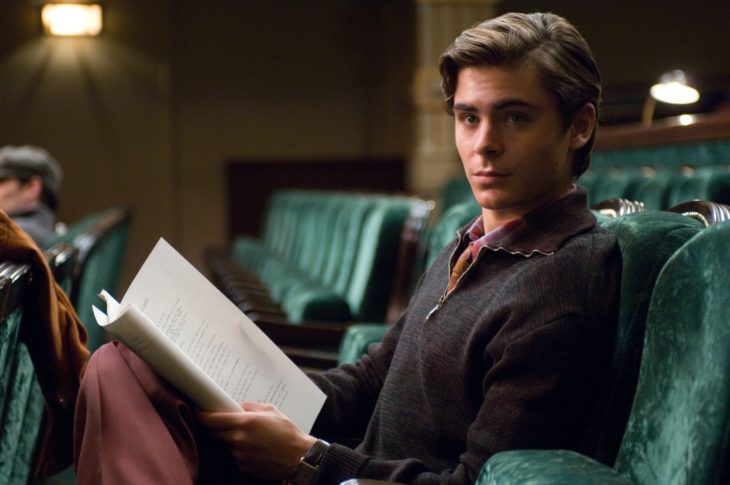 Zac Efron sentado en un sofá leyendo 