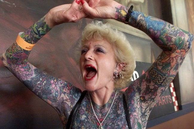 Abuela alzando los brazos llenos de tatuajes y gritando 
