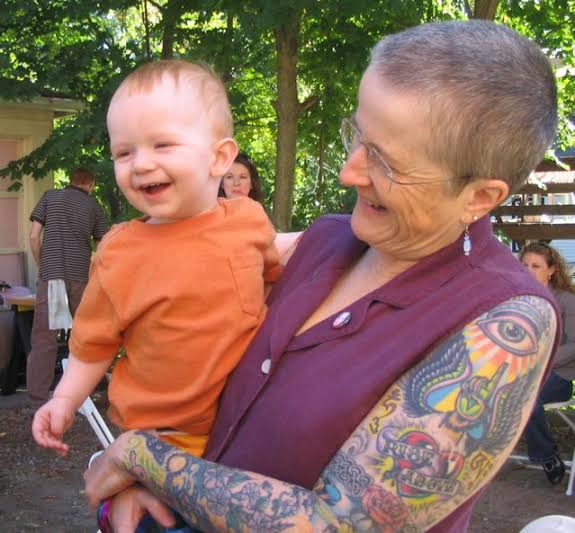 Abuela cargando a su nieto y mostrando su brazo con tatuajes