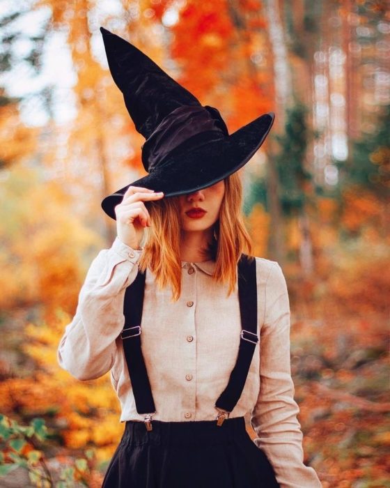 Chica en un bosque repleto de hojas anaranjadas llevando un sombrero de pico 