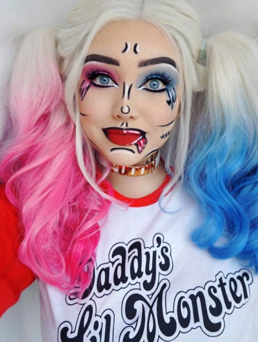 Disfraz de Halloween de comic pop art; chica de ojos azules de cabello rubio con peinado de coletas, maquillada estilo historieta de villana Harley Quinn con cabello azul y rosa