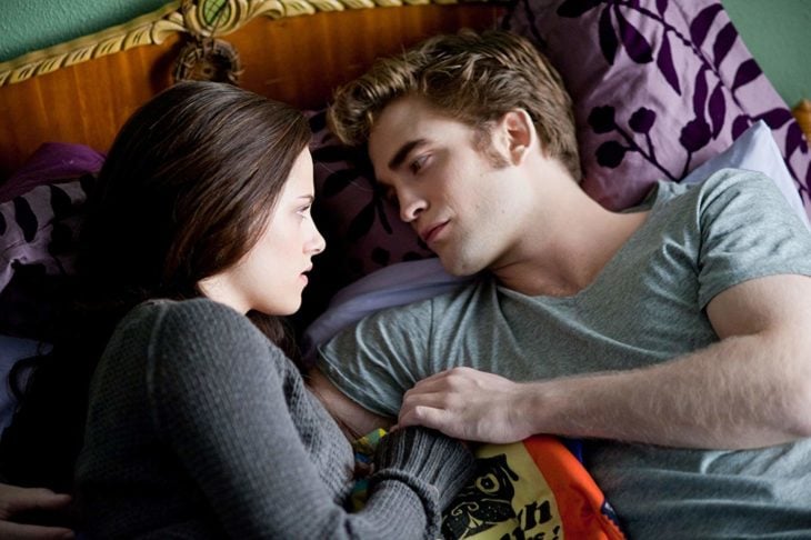 Edward Cullen recostado en la cama de Bella mientras está charlando con ella 